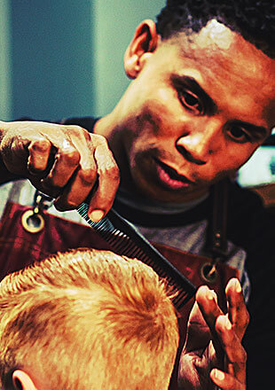 Barber pria sedang memotong rambut pelanggan muda di salon.