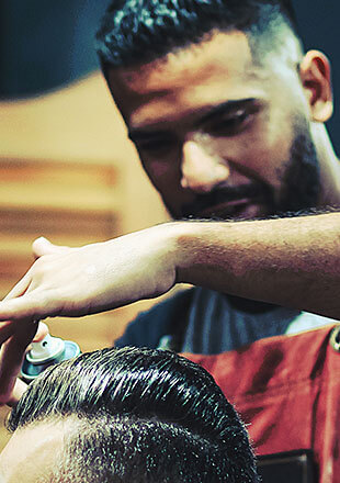 Pekerja barbershop sedang memotong rambut pelanggan dengan alat cukur listrik.